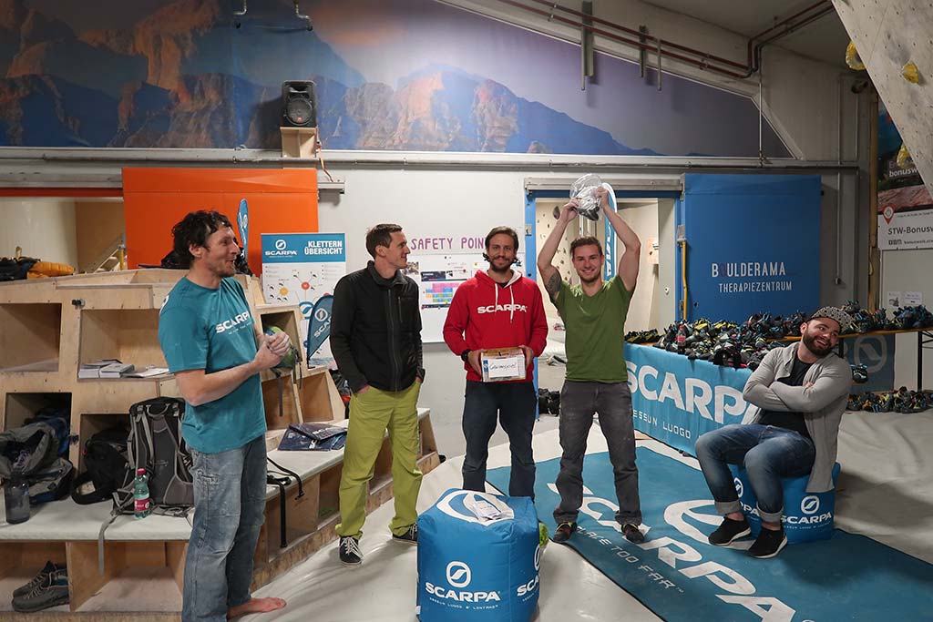 Das Bild zeigt das Event Sponsoring von Bolting.eu. Bei einer Siegerehrung in einer Boulderhalle stehen die Top 3 Platzierten mit Firmenvertretern in Bildmitte. Der Sieger hält einen Preis in die Höhe.
