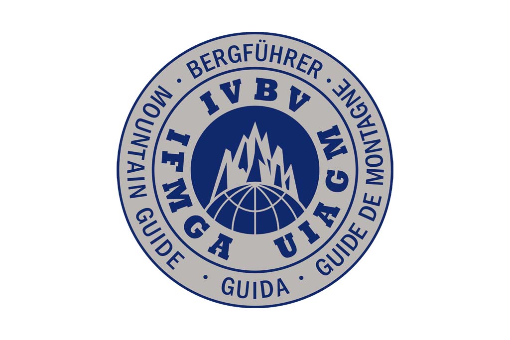 Das Bild zeigt das internationale Logo des Bergführerverbandes. Ein Kreis mit drei blauen Ringen, in jedem Ringsegment der NAme der Vereinigung bzw. im Zentrum ein Umriss eines Berges.