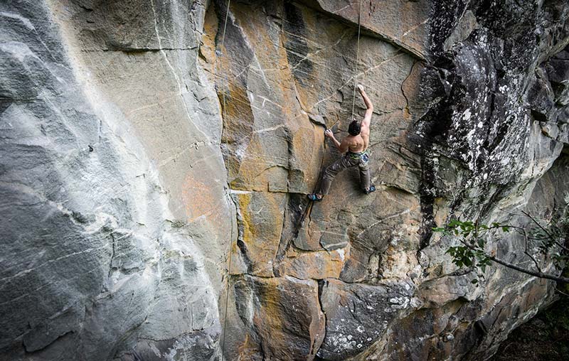 Das Bild zeigt einen Kletterer im Top Rope in einer Felswand. Er will eine Kletterroute mit Bohrhaken einrichten und probiert daher die besten Klipp Positionen aus. Das Bild veraunschaulicht diesen wichtig Schritt.