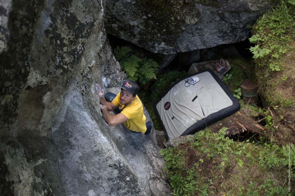 Das Bild zeigt ein Beispiel für den Boulderausrüstung Gegenstand Bouldermatte. Unter einem Boulderer mit Schildkappe und gelbem Shirt befindet sich ein Moon Crashpad.
