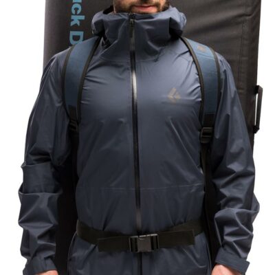 Das Bild zeigt einen Boulderer stehend it dunkelblauer Jacke, am Rücken trägt er ein Black Diamond Drop Zone Crashpad.