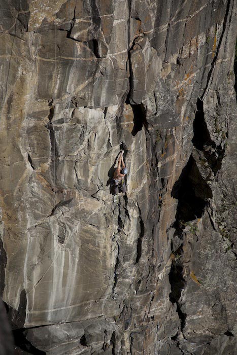 Das Bild zeigt einen Kletterer in einerFelswand mit markanten Riss wo er einen Klemmkeil legt.