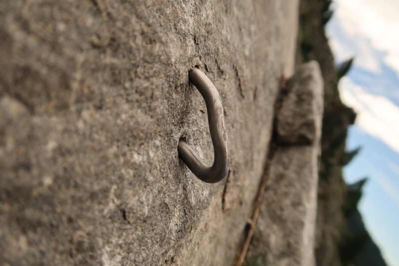 Das Bild zeigt einen umgebogenen Verbundhaken durch Steinschlag auf einer grauen Felsplatte.