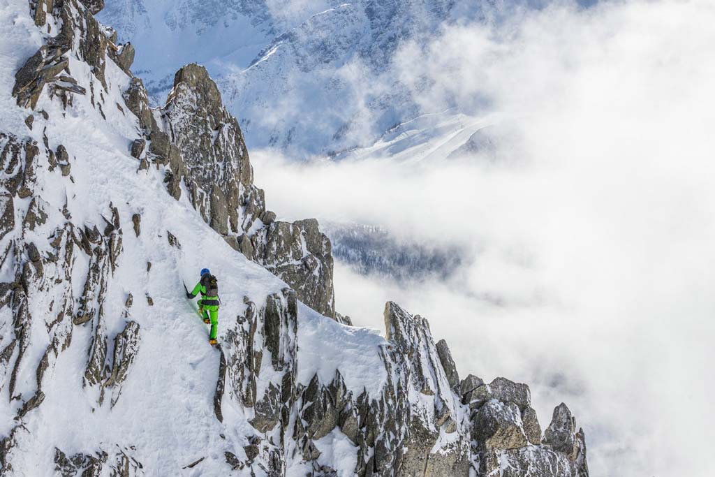 Alpinist in verschneitem Gelände mit Berggipfeln und blauem Himmel.